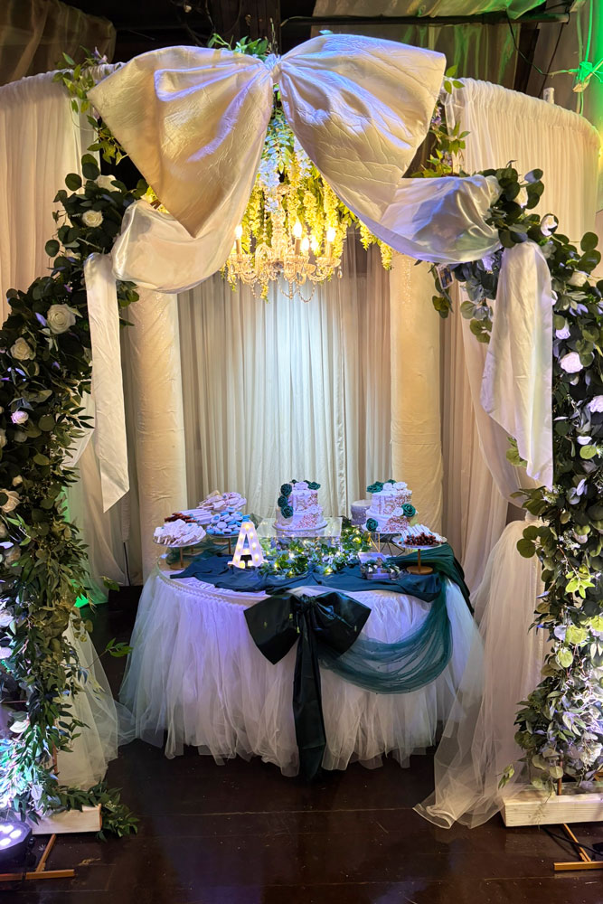 Cake table canope with greenery and beautiful cake table dcorations including a two bows.