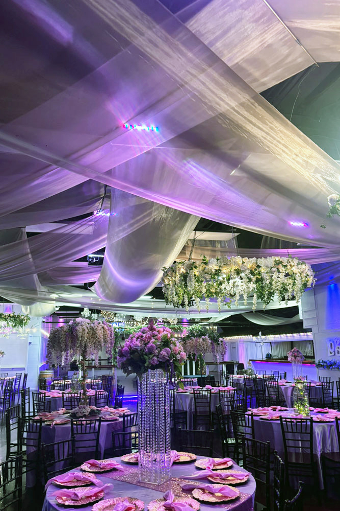 Ceiling fabric inside our beautiful and well lit ballrooom with accent lighting and guest tables that are already set up.