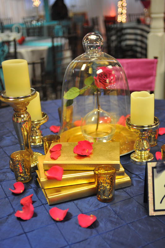 Modern glass bell jar centerpiece with lighting accents on  top of books for a beauty and the beast event table at The Chateau at Forest Park class