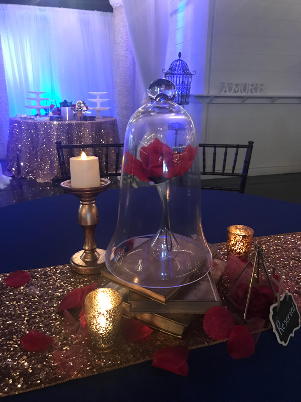 Classic glass bell jar centerpiece with a rose and lighting accents atoop books for an elegant beauty and the beast table at The Chateau at Forest Park