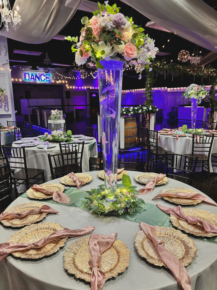 Whimsical tall glass centerpiece design with floating butterfly elements, floral accents, and accent lighting