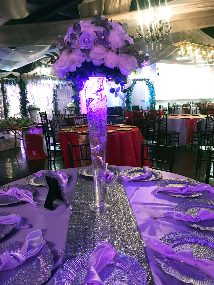 Whimsical tall pilsner vase centerpiece design with floating butterfly elements, floral accents, and accent lighting