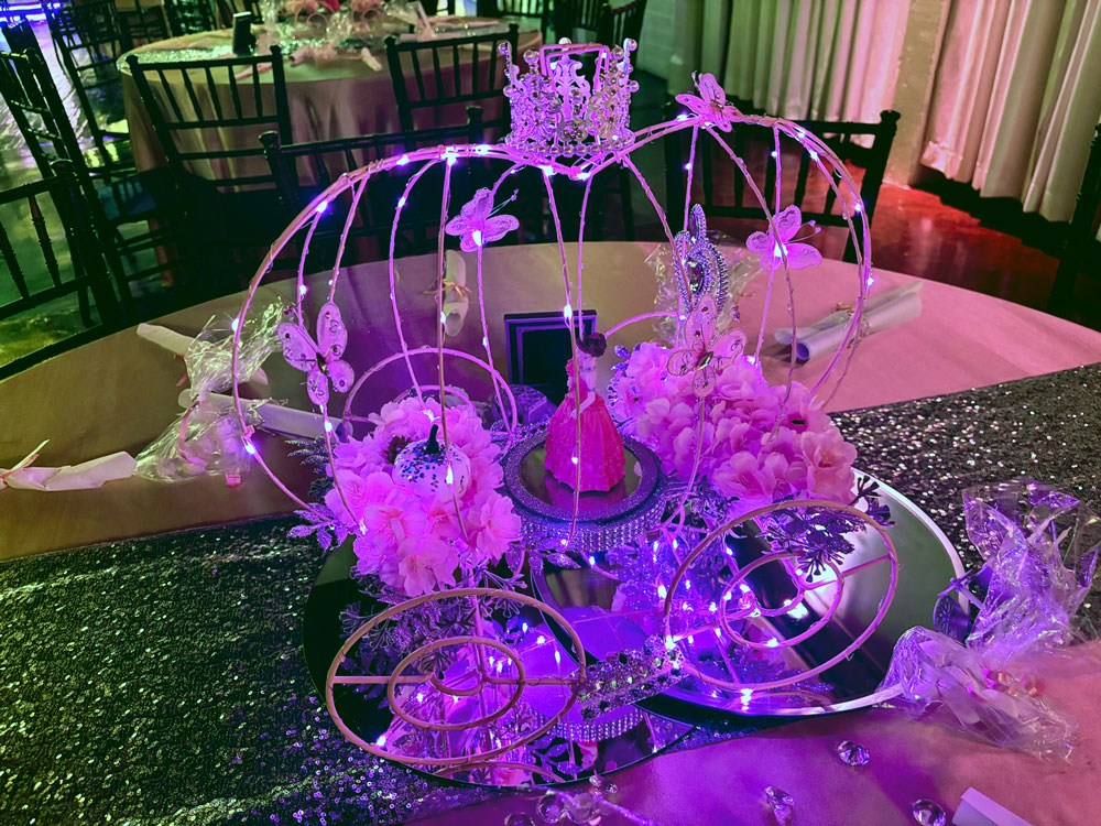 Cinderella-style quinceañera coach centerpiece featuring dramatic details, twinkle lighting, and elegant design
